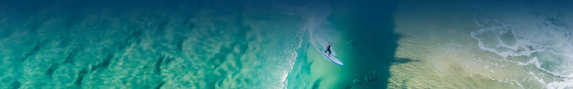 A surfer gracefully rides a wave at Capricorn Beach, captured from an aerial perspective.