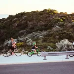 A family cycling along a Capricorn Beach street at sunset, one of the things to do in Yanchep.