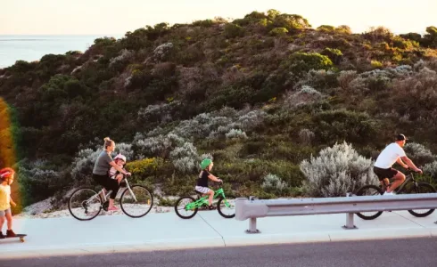 A family cycling along a Capricorn Beach street at sunset, one of the things to do in Yanchep.