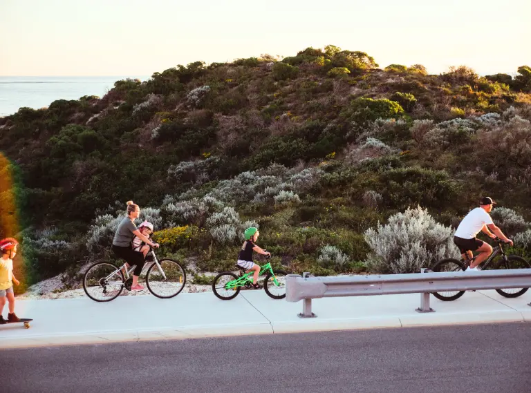 A family cycling along a Capricorn Beach street at sunset, one of the things to do in Yanchep.